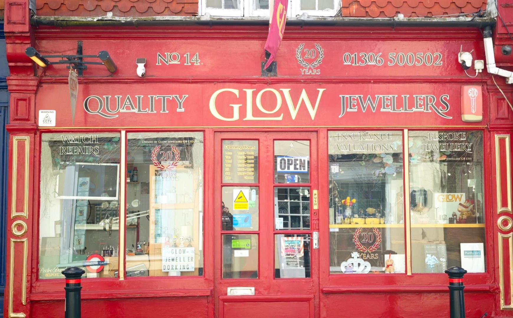 Glow Jewellers’ red shopfront and gold lettering on West Street, Dorking, in daylight with the OPEN sign lit in the door