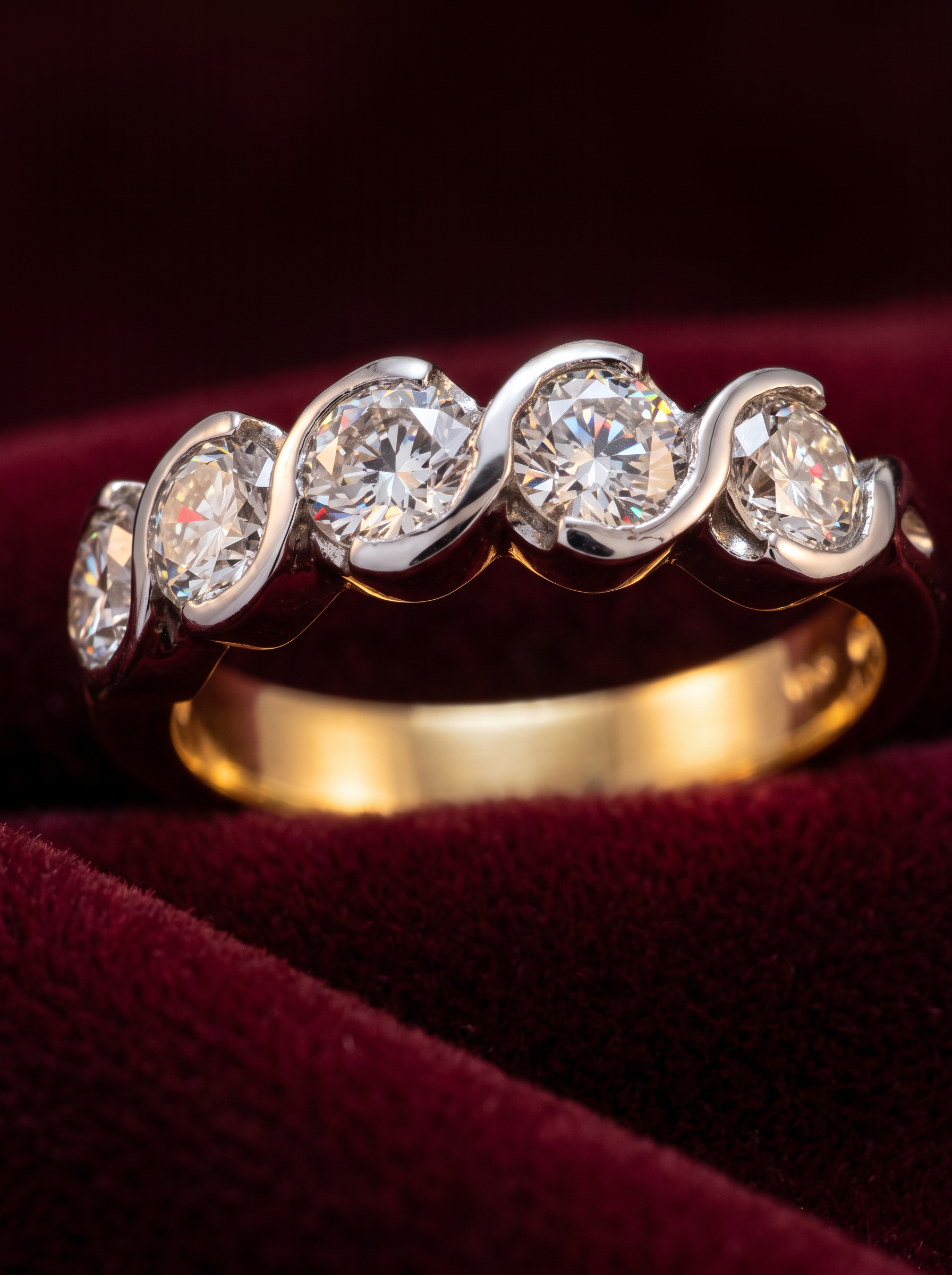 A gold and white-gold swirl diamond eternity ring on burgundy velvet, made by Pedro