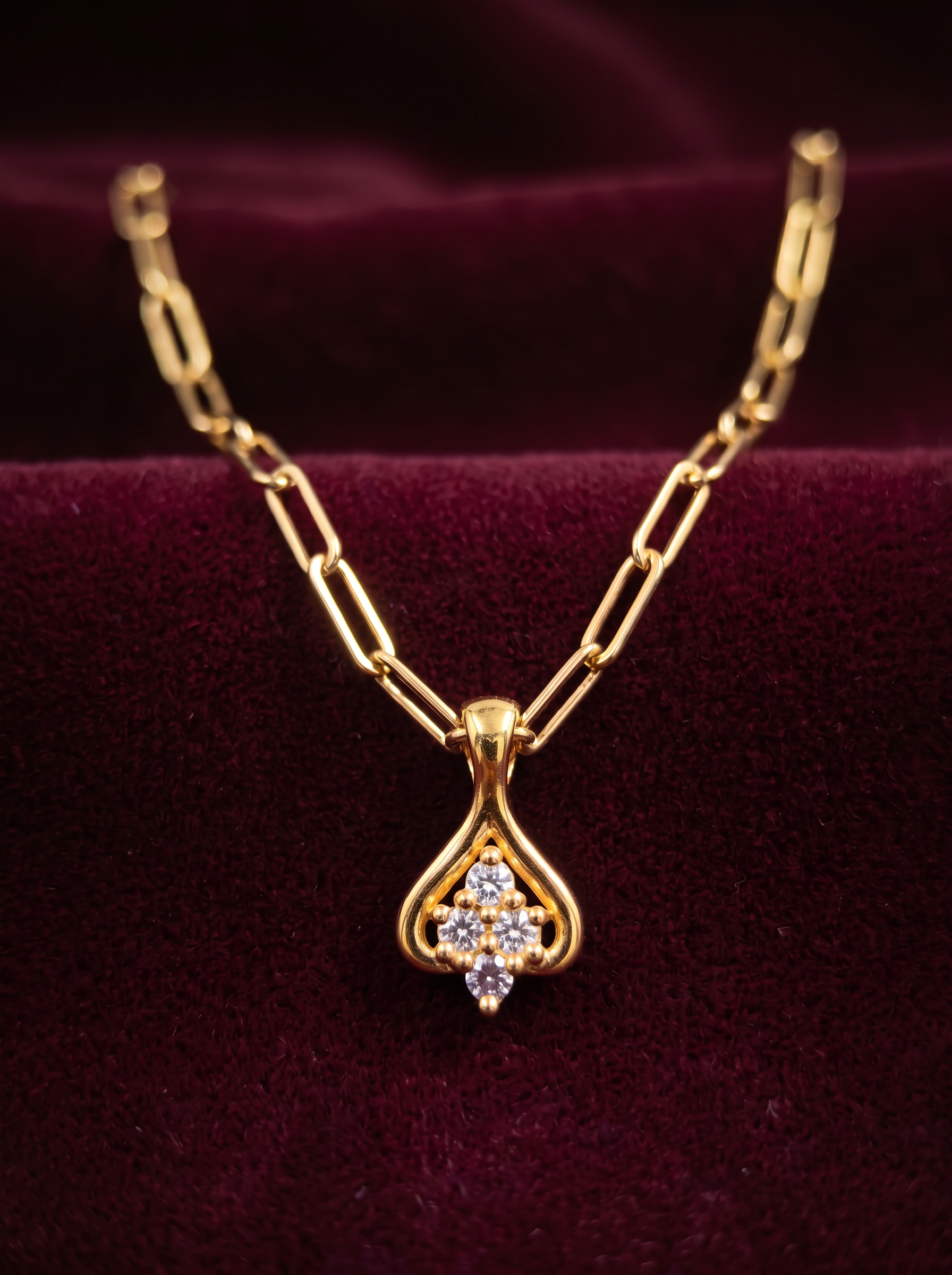 A yellow gold paperclip-chain pendant set with four round stones in a cluster, on deep burgundy velvet — commissioned for a customer